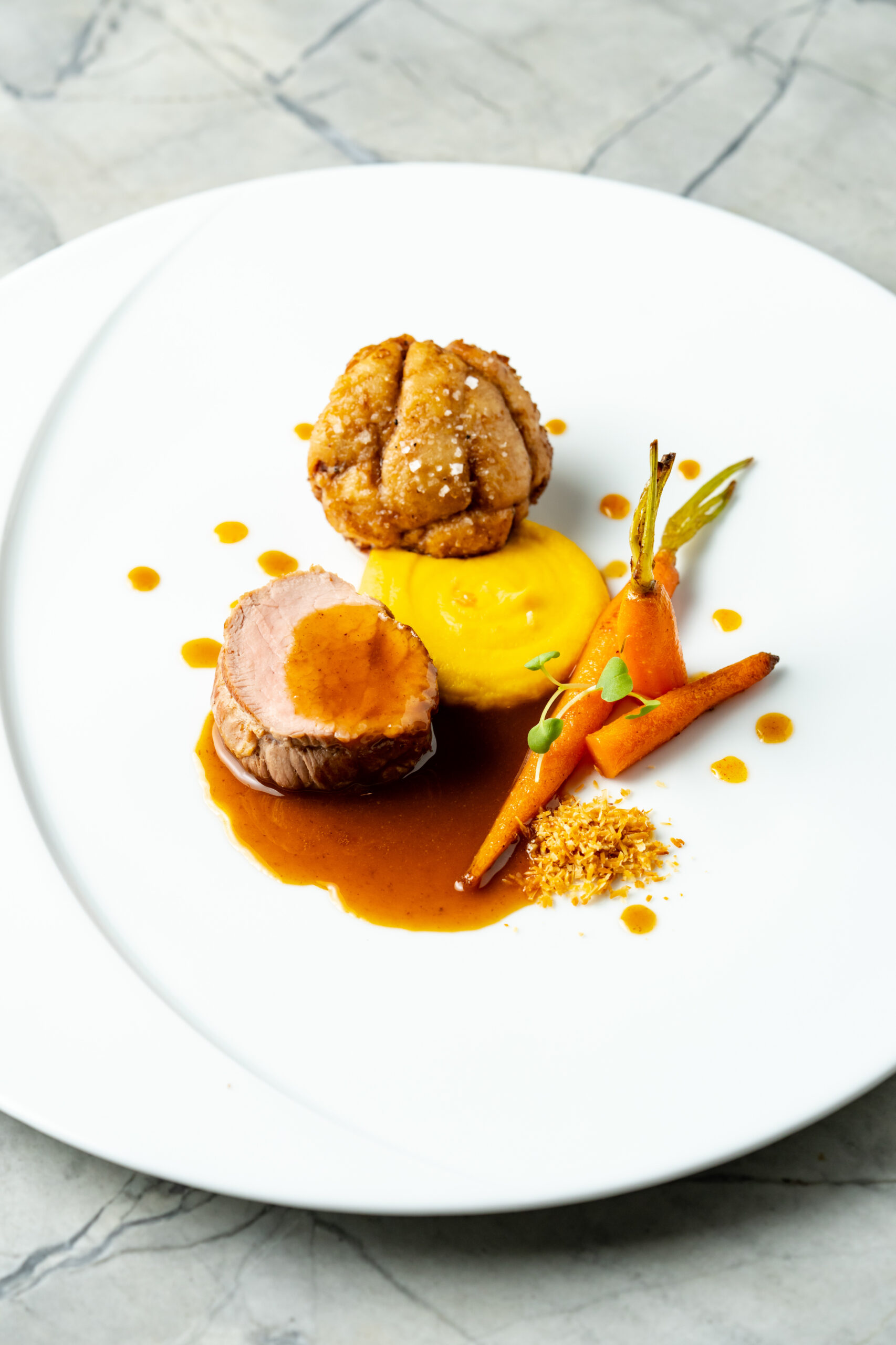 Plated French main course with roasted meat, carrots, and pan sauce